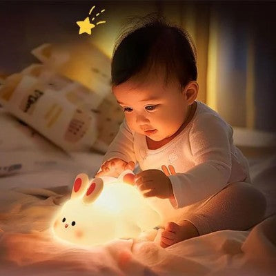 Bébé émerveillé touchant une veilleuse lapin lumineuse.