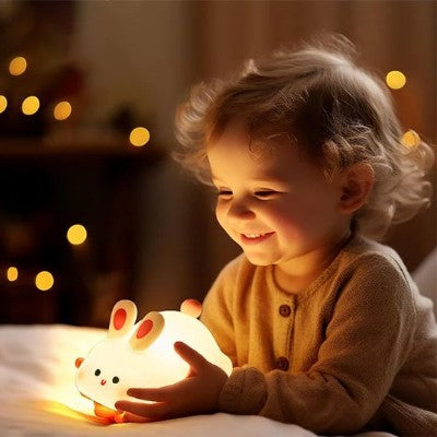 Enfant souriant en tenant une veilleuse lapin réconfortante.