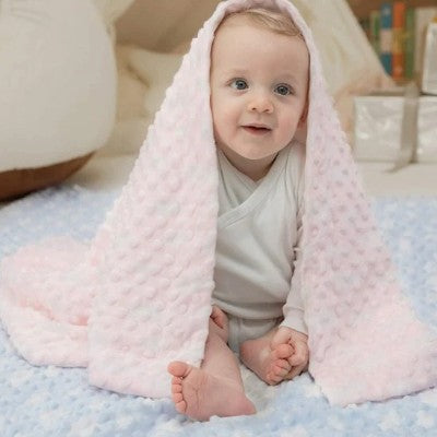 couverture bébé rose enveloppant bébé assis dans decor cosy