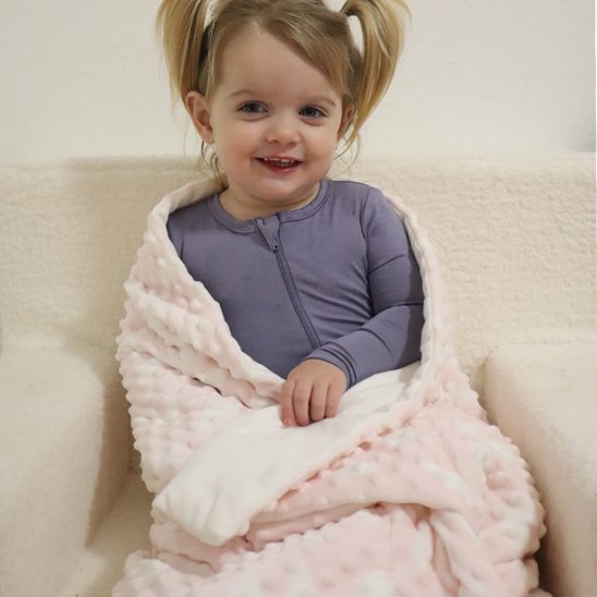 couverture bébé rose et blanche enveloppant enfant souriant