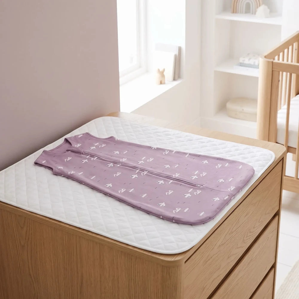 Gigoteuse bébé fille mauve à oiseaux blancs posée à plat sur une commode à langer