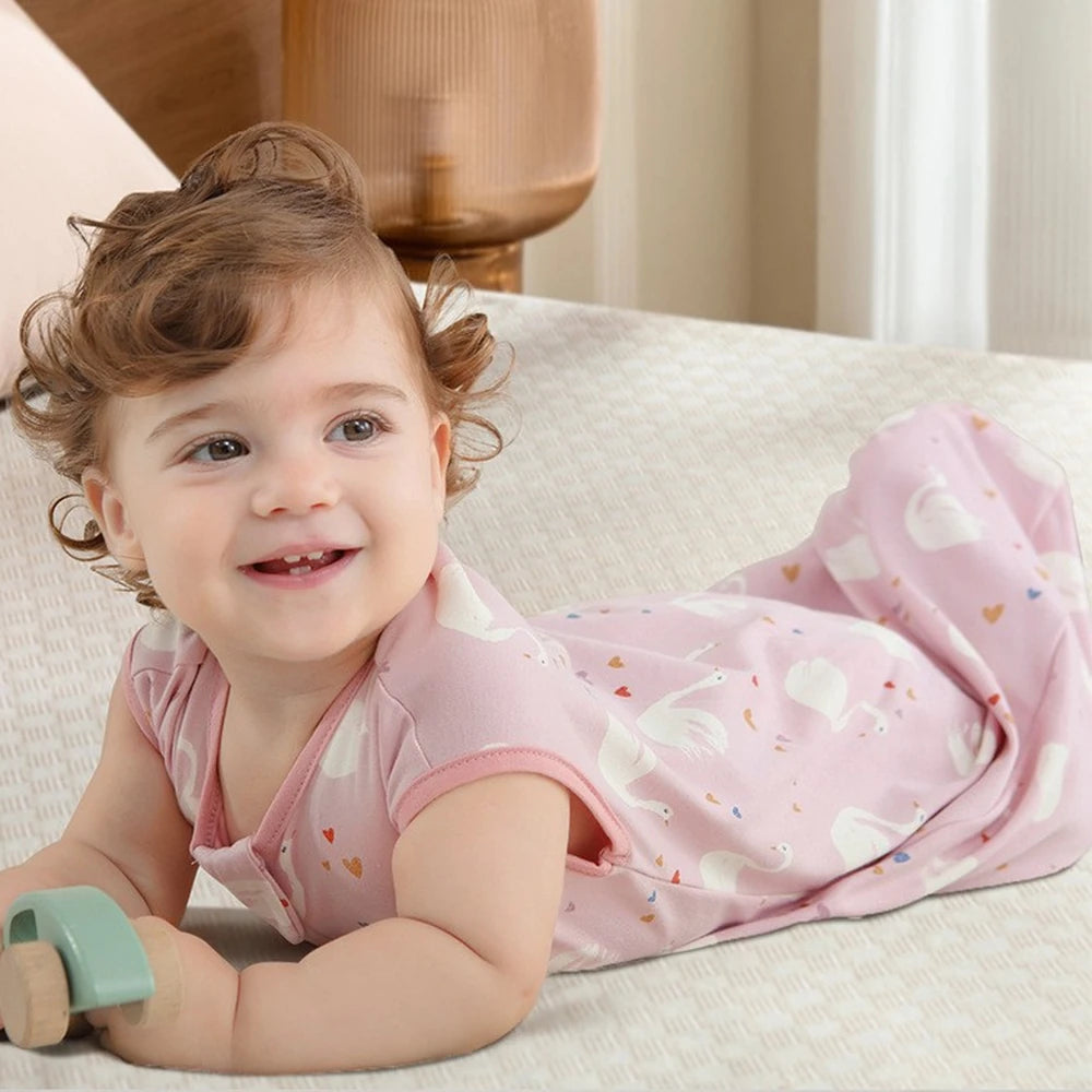Bébé éveillé à plat ventre, souriant, en gigoteuse rose à cygnes
