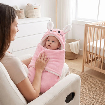 Bébé éveillé dans le nid d'ange bébé rose à capuche lapin, dans les bras de sa maman assise dans un fauteuil
