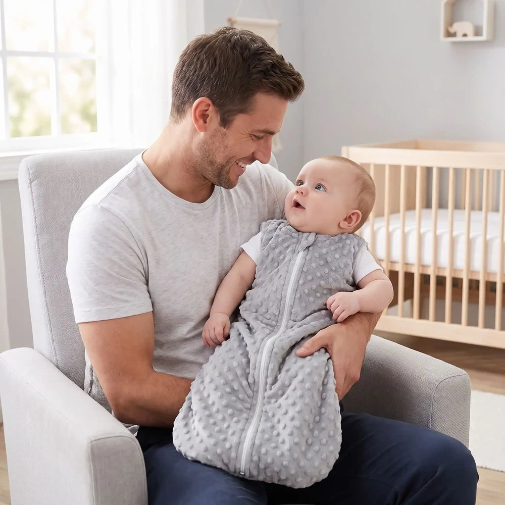 Bébé éveillé dans les bras de son papa, en turbulette naissance grise à pois en relief